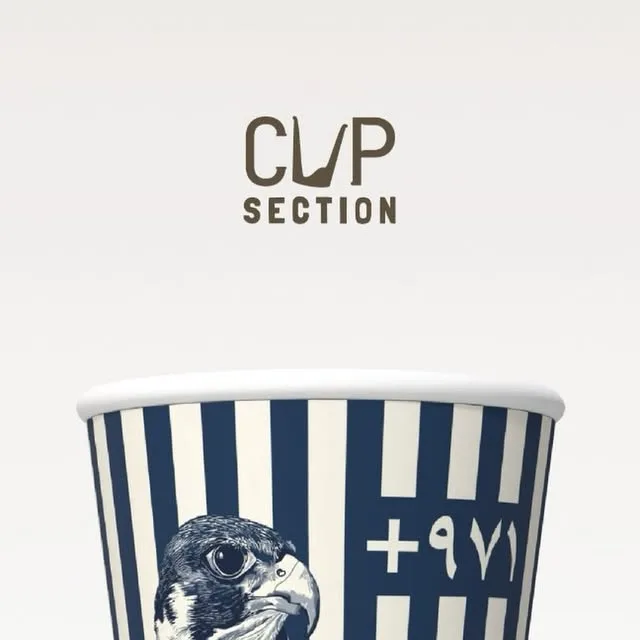 Paper cup with navy and cream vertical stripes, a pen-drawn falcon head and the UAE dial code +971 in Arabic numerals.
